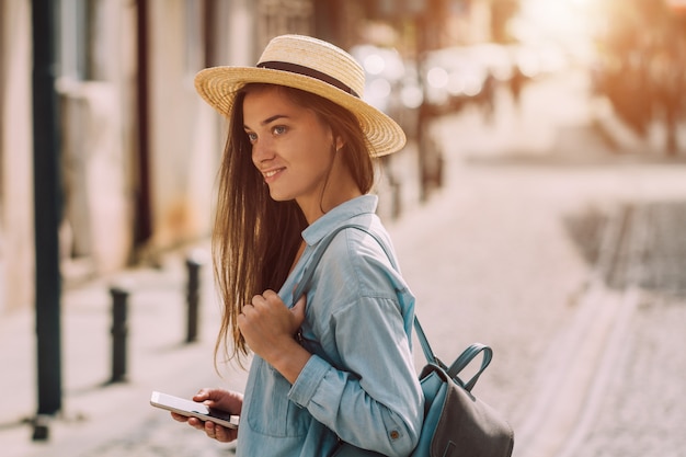 Voyager femme au chapeau avec sac à dos et téléphone marchant le long de la rue d'une ville européenne. Vacances et voyages