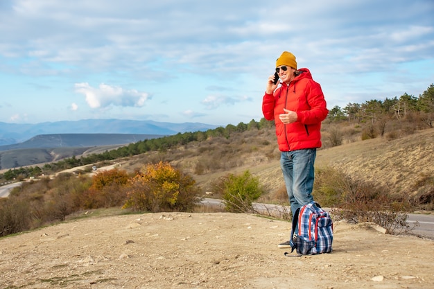 Un voyageur adulte parle au téléphone et rit en se tenant debout dans les montagnes.