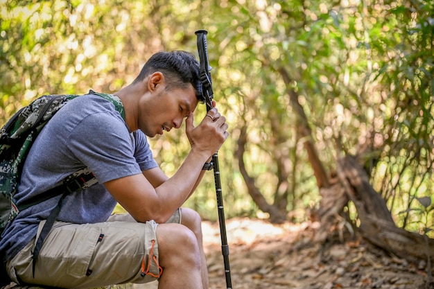 Un voyageur asiatique fatigué avec un équipement de trekking est assis sur une bûche en bois se reposant pendant le trekking