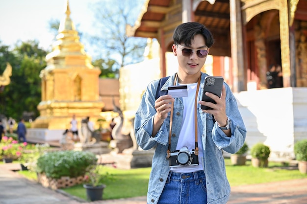 Voyageur asiatique portant des lunettes de soleil regardant l'écran de son smartphone tenant une carte de crédit