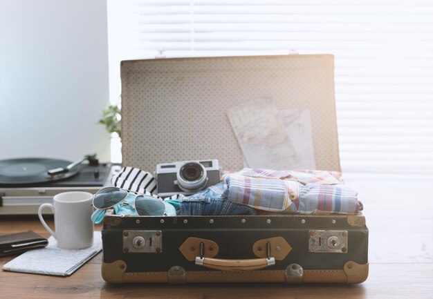 Photo voyageur emballant ses bagages avant de partir en vacances valise vintage ouverte avec vêtements appareil photo et lecteur de disques vintage voyage et concept de renaissance rétro