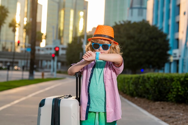 Voyageur enfant avec valise partant en vacances Garçon touristique en voyage de vacances enfants concept Joli garçon avec valise sur fond de rue de la ville