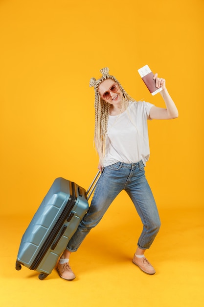 Voyageur femme blonde avec grande valise, passeport et billet d'avion