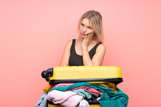 Voyageur femme avec une valise pleine de vêtements sur mur rose isolé malheureux et frustré