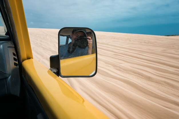 Voyageur d'homme prenant une photo sur la voiture à quatre roues jaune sur le désert rayé