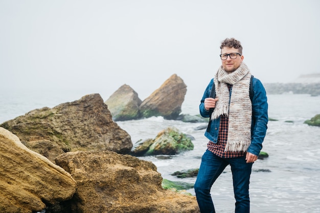 Voyageur homme avec un sac à dos debout sur un rocher contre une belle mer avec des vagues