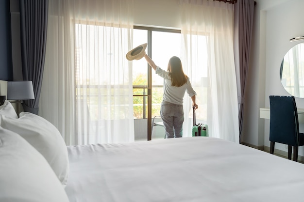 Voyageur de jeune femme avec des bagages regardant la vue dans la chambre d'hôtel en vacances d'été