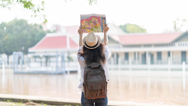 Voyageur de jeune femme avec sac à dos et chapeau regardant la carte avec fond de temple Thaïlande