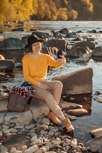 Voyageur de la jeune femme avec un téléphone portable dans les mains assis sur un rocher près de la nature de la rivière