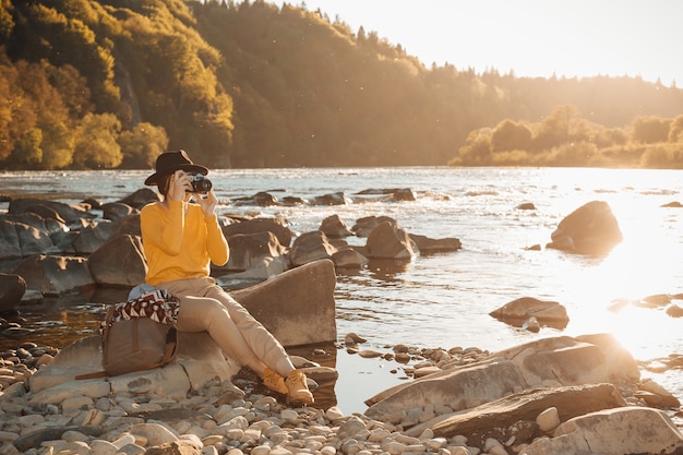 Voyageur de la jeune femme avec un téléphone portable dans les mains assis sur un rocher près de la nature de la rivière