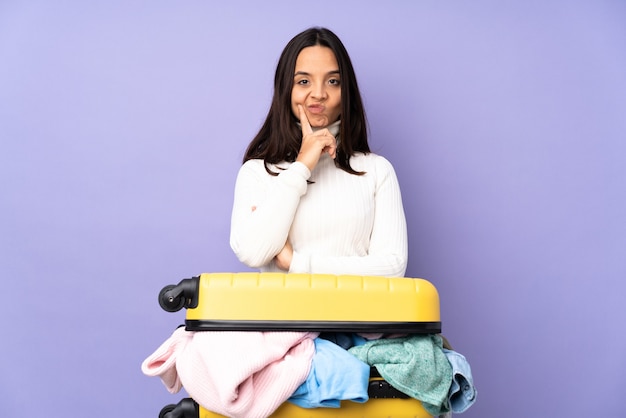 Voyageur jeune femme avec une valise pleine de vêtements sur violet isolé et à l'avant