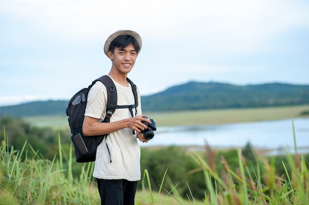 Voyageur de jeune homme asiatique avec appareil photo numérique sac à dos regarde la caméra avec fond de lac belle nature.