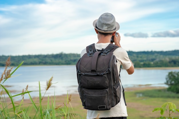 Voyageur jeune homme asiatique portant bonnet tricoté avec sac à dos en prenant une photo et en regardant le lac étonnant