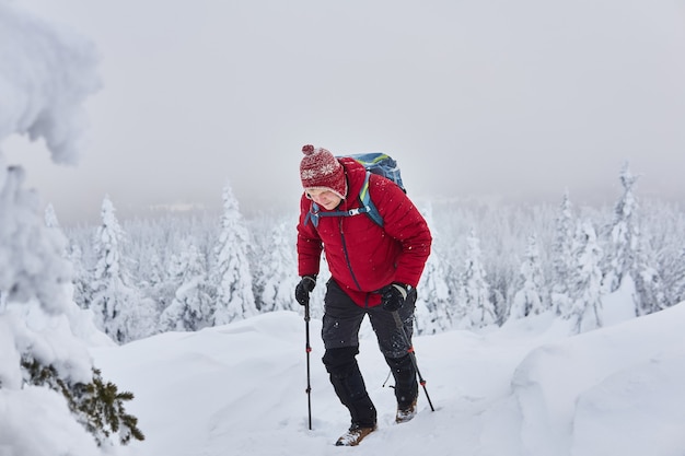 Le voyageur masculin monte une montagne en hiver pendant une chute de neige