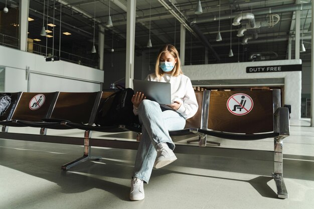 Voyageur en masque assis dans la chaise du hall de l'aéroport avec signe de distanciation sociale