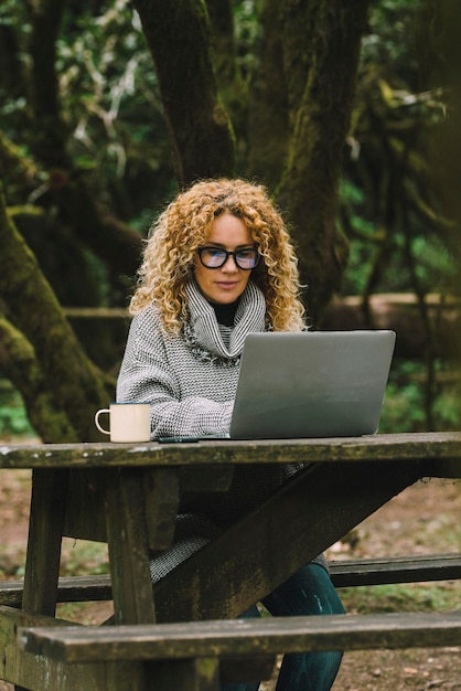 Voyageur nomade numérique concept de travail style de vie Alternative à l'extérieur du bureau dans la nature Jolie femme travaillant intelligemment sur un ordinateur portable assis dans les bois Femmes bénéficiant d'une connexion en ligne