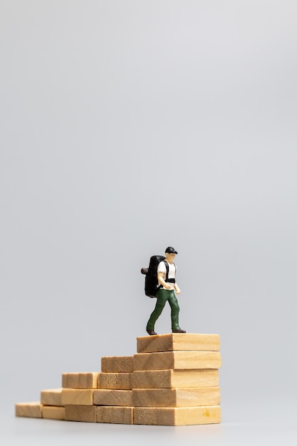 Voyageur de personnes miniatures debout sur un bloc de bois sur fond gris. Concept de voyage et d'aventure