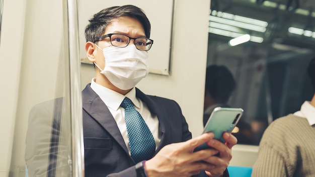 Voyageur portant un masque facial tout en utilisant un téléphone mobile dans un train public. Maladie à coronavirus ou épidémie de pandémie COVID 19 et problème de mode de vie en ville urbaine dans le concept de navettage aux heures de pointe.