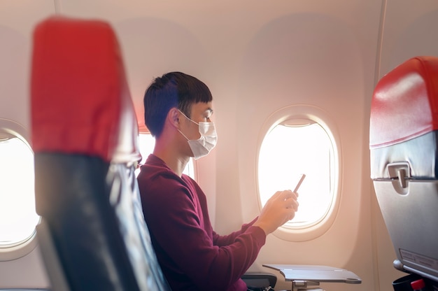 Un voyageur portant un masque de protection à bord de l'avion à l'aide d'un smartphone, voyage sous la pandémie de Covid-19