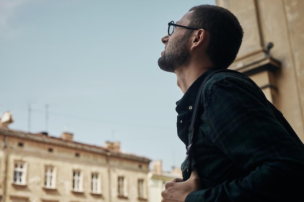 Voyageur à la recherche d'une grande ville, d'un voyage et d'un concept de mode de vie actif. L'homme touristique barbu avec sac à dos profite d'une belle vue panoramique sur la ville européenne moderne.