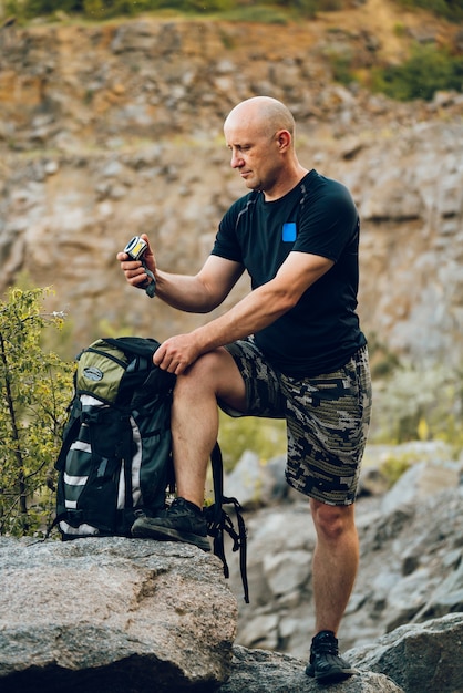 Un voyageur regarde la boussole dans sa main et tient un sac à dos à côté de lui