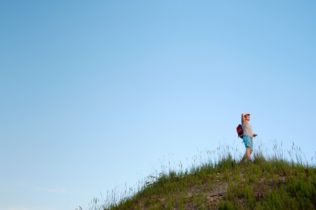 Voyageur avec sac à dos orange restant dans les collines sur fond de ciel bleu et à l'avenir