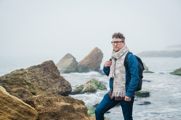 le voyageur avec un sac à dos se tient sur un rocher contre une belle mer avec des vagues