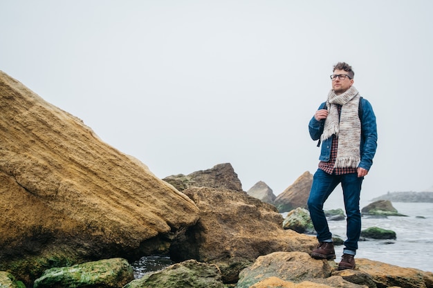 le voyageur avec un sac à dos se tient sur un rocher contre une belle mer avec des vagues