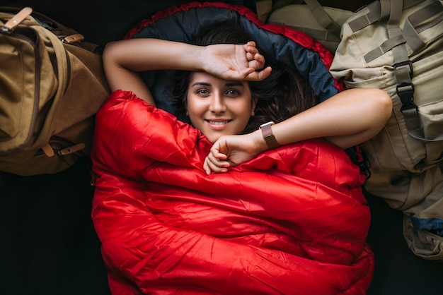 Le voyageur se repose dans un sac de couchage. Concept de repos. Un touriste se repose dans une tente. Femme relaxante dans un sac de couchage. Voyage, concept de camping, aventure. Bonne voyageuse souriante. Le voyageur