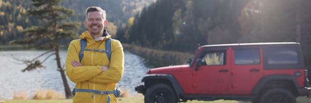 Voyageur souriant debout et regardant la voiture tout-terrain et le lac avec montagne et forêt