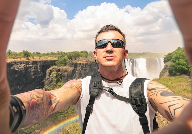 Voyageur avec des tatouages prenant selfie à Victoria Falls