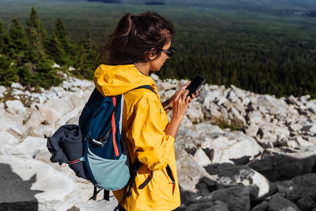 Un voyageur avec un téléphone, gros plan. Une touriste vêtue d'une veste jaune avec un sac à dos tient un téléphone dans ses mains. Femme de randonnée utilisant un téléphone intelligent, un concept de voyage et de mode de vie actif. Espace de copie