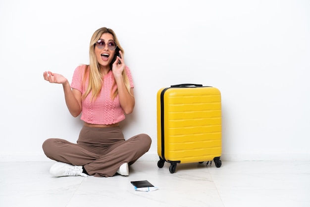 Voyageur uruguayen femme assise sur le sol isolé sur fond blanc en gardant une conversation avec le téléphone mobile avec quelqu'un