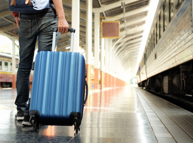 Voyageur avec une valise bleue attend le train.