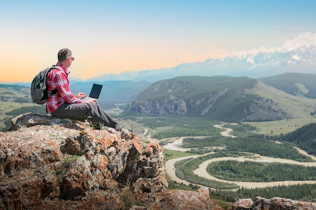 Les voyageurs masculins travaillent à distance sur un ordinateur netbook et profitent du paysage naturel des montagnes au coucher du soleil.