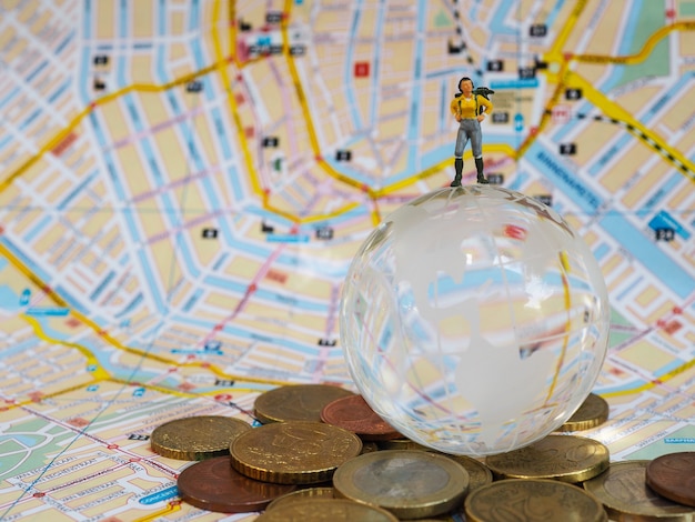 Les voyageurs miniatures ou les routards se tiennent sur un globe de verre, des pièces en euros et une carte.