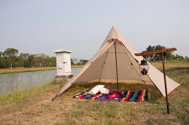 Les voyageurs thaïlandais et étrangers voyagent en visite et tentent de camper avec une lanterne antique sur un parc en herbe à côté d'un canal d'irrigation à la campagne rurale de la ville de Bangbuathong de Nonthaburi à Bangkok en Thaïlande