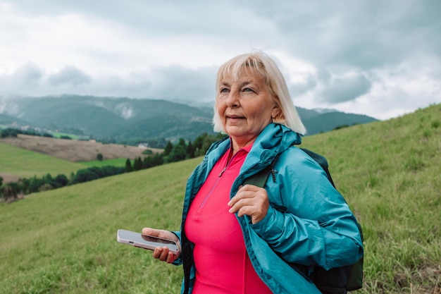 Une voyageuse âgée caucasienne utilise un téléphone portable pour prendre un selfie alors qu'elle voyage seule en montagne.