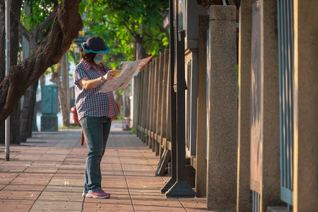 Une voyageuse asiatique porte un masque de protection à la recherche d'une carte sur le trottoir dans un espace public