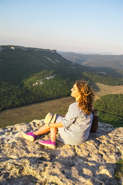 Une voyageuse est assise au sommet d&#39;une montagne et tient son chapeau