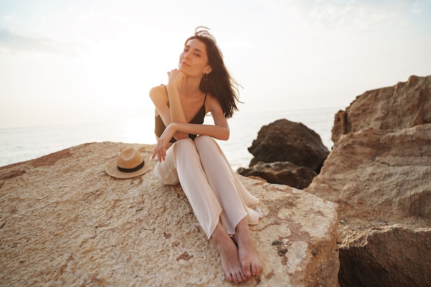 Voyageuse de femme assise près de la mer sur la falaise profitant d'une vue sur la mer et la nature