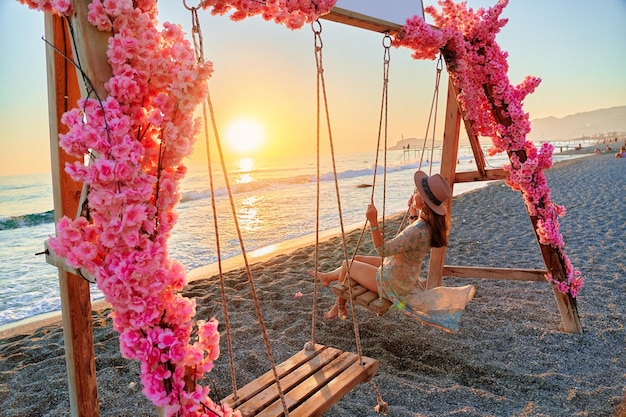 Une voyageuse heureuse et insouciante se promène sur une balançoire au bord de la mer au coucher du soleil et profite d'un moment de vie magnifique Vacances à la plage et retraite d'escapade pour personne