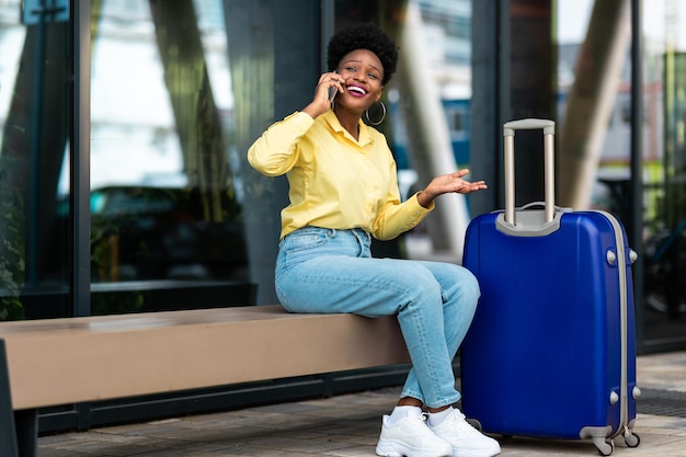 Une voyageuse noire parlant sur un téléphone portable assis en zone urbaine