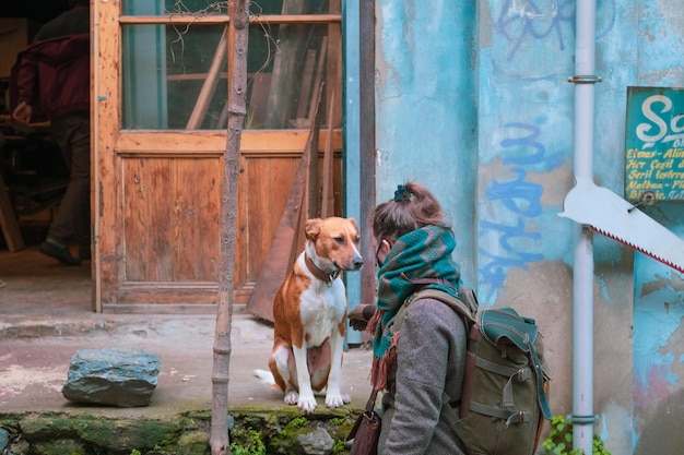 Une voyageuse avec un sac à dos caresse un joli chien rouge contre l'ancien bâtiment