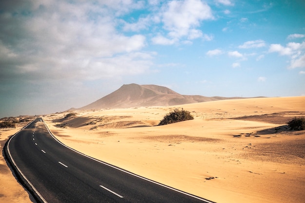 Voyagez sur le concept de route avec une longue route goudronnée au milieu des dunes, du désert de sable et des montagnes pour l'aventure et des lieux pittoresques alternatifs pour des vacances ou une expérience de style de vie d'aventure