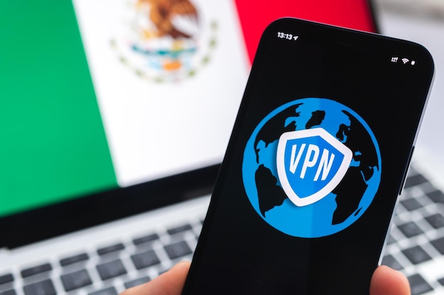 VPN au Mexique Concept Internet sécurisé et sécurisé Confidentialité Main avec téléphone mobile et application VPN Drapeau et ordinateur portable sur la photo d'arrière-plan