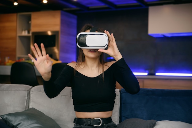 VR. Excité fille millénaire utilisant un casque de réalité virtuelle jouant à un jeu vidéo en intérieur. Focus sélectif