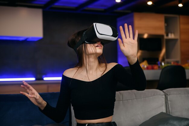 VR. Excité fille millénaire utilisant un casque de réalité virtuelle jouant à un jeu vidéo en intérieur. Focus sélectif