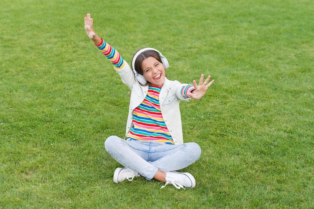 Vrai bonheur petite fille sur l'herbe verte enfant profiter de la chanson dans le parc nature enfance heureuse concept utiliser un appareil numérique dans la vie moderne écolière se détendre en plein air enfant heureux écouter de la musique dans les écouteurs
