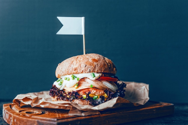 Un vrai burger sur un fond en bois. Avec une grosse escalope juteuse, sauce au fromage tendre et moutarde. Rustique